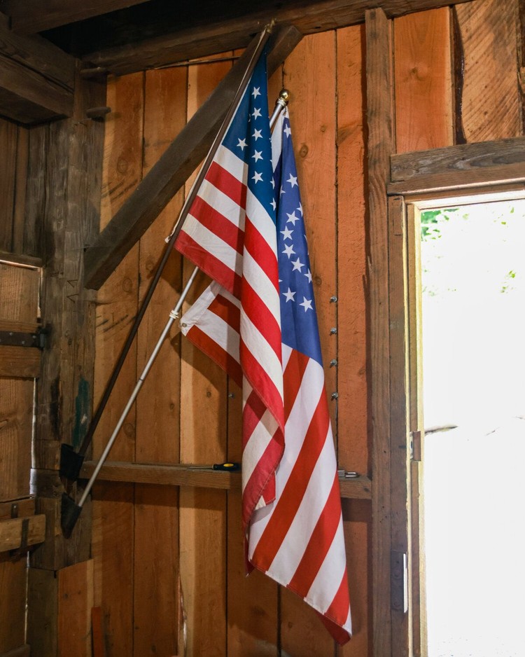 Two different versions of the American flag hang by the doorway of the Cedar Creek Grist Mill.