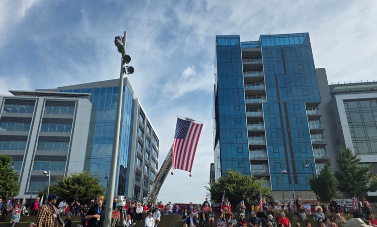 A flag is displayed high in the sky in front of buildings along the Vancouver Waterfront